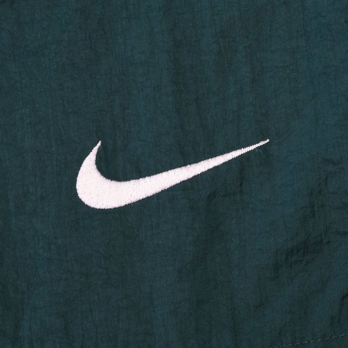 Close-up of small white Nike Swoosh embroidery on green swim trunks