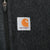 Close-up of Carhartt logo patch beside the chest pocket zipper on dark grey fleece