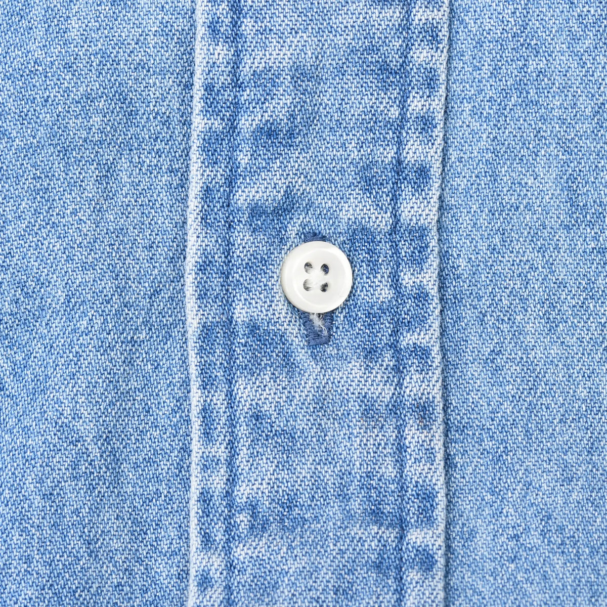 Close-up of white four-hole button and stitching on blue denim shirt placket