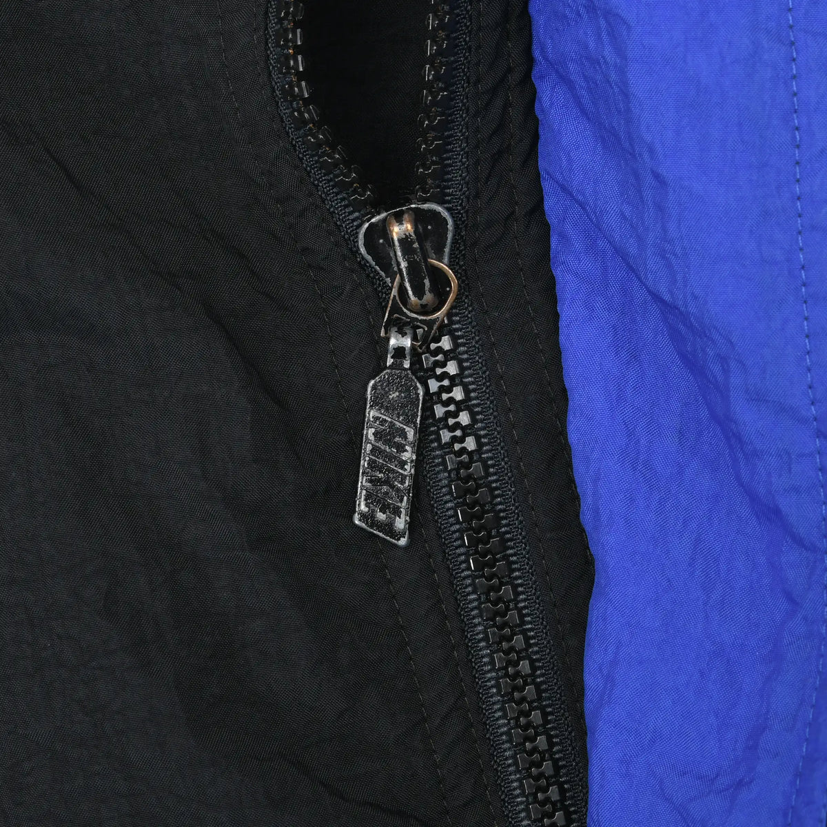 Close-up of black front zipper and metal pull beside the windbreaker's blue panel