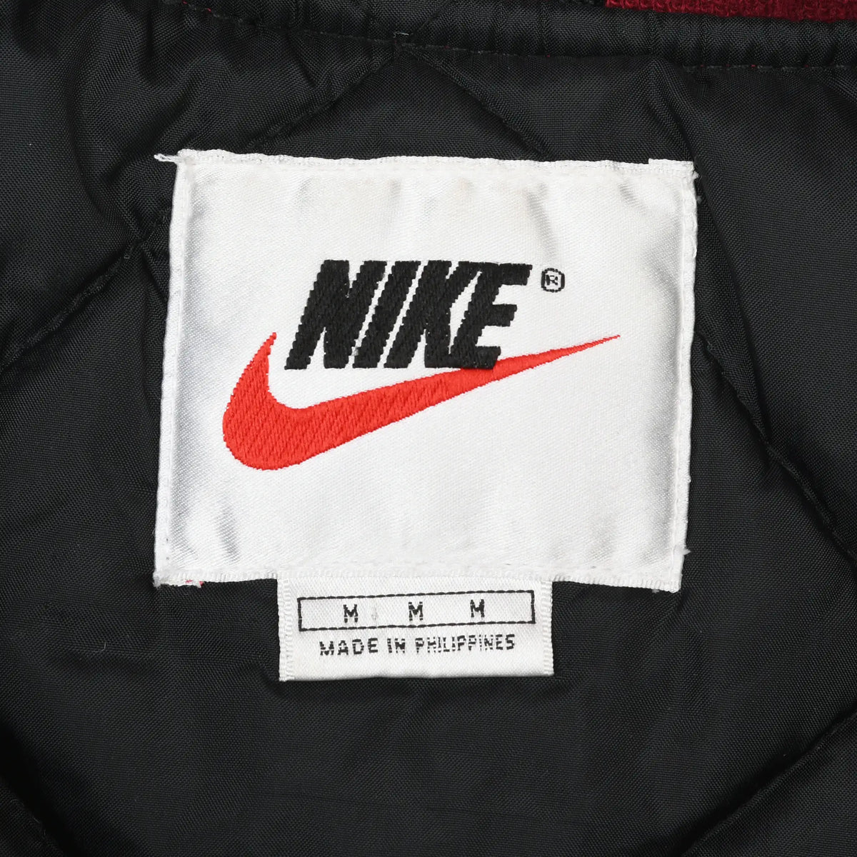 Nike neck label with black logo, red Swoosh, medium size markings, and Made in Philippines text