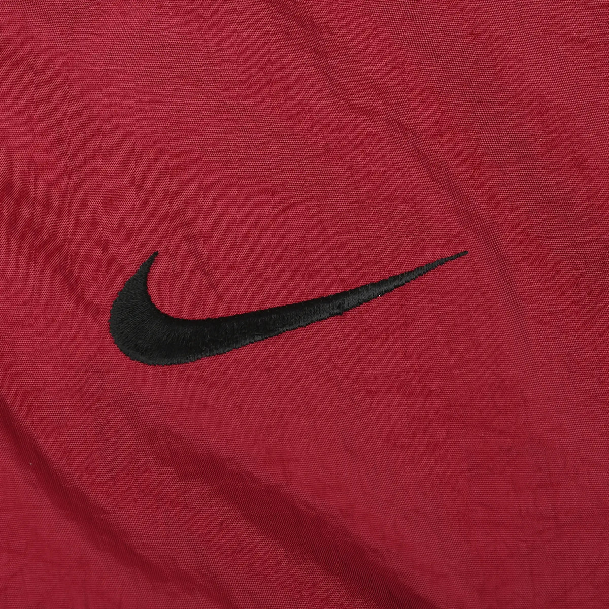 Close-up of small black Nike Swoosh embroidery on burgundy jacket front