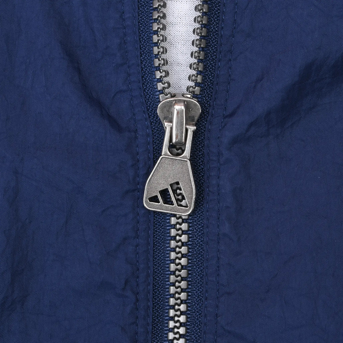 Close-up of silver Adidas logo zipper pull on navy jacket fabric