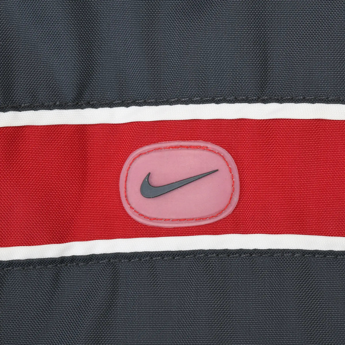 Close-up of Nike Swoosh patch on the red and white chest stripe of the black jacket