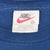 Nike neck tag on blue T-shirt showing red Swoosh, medium size, and Made in USA text