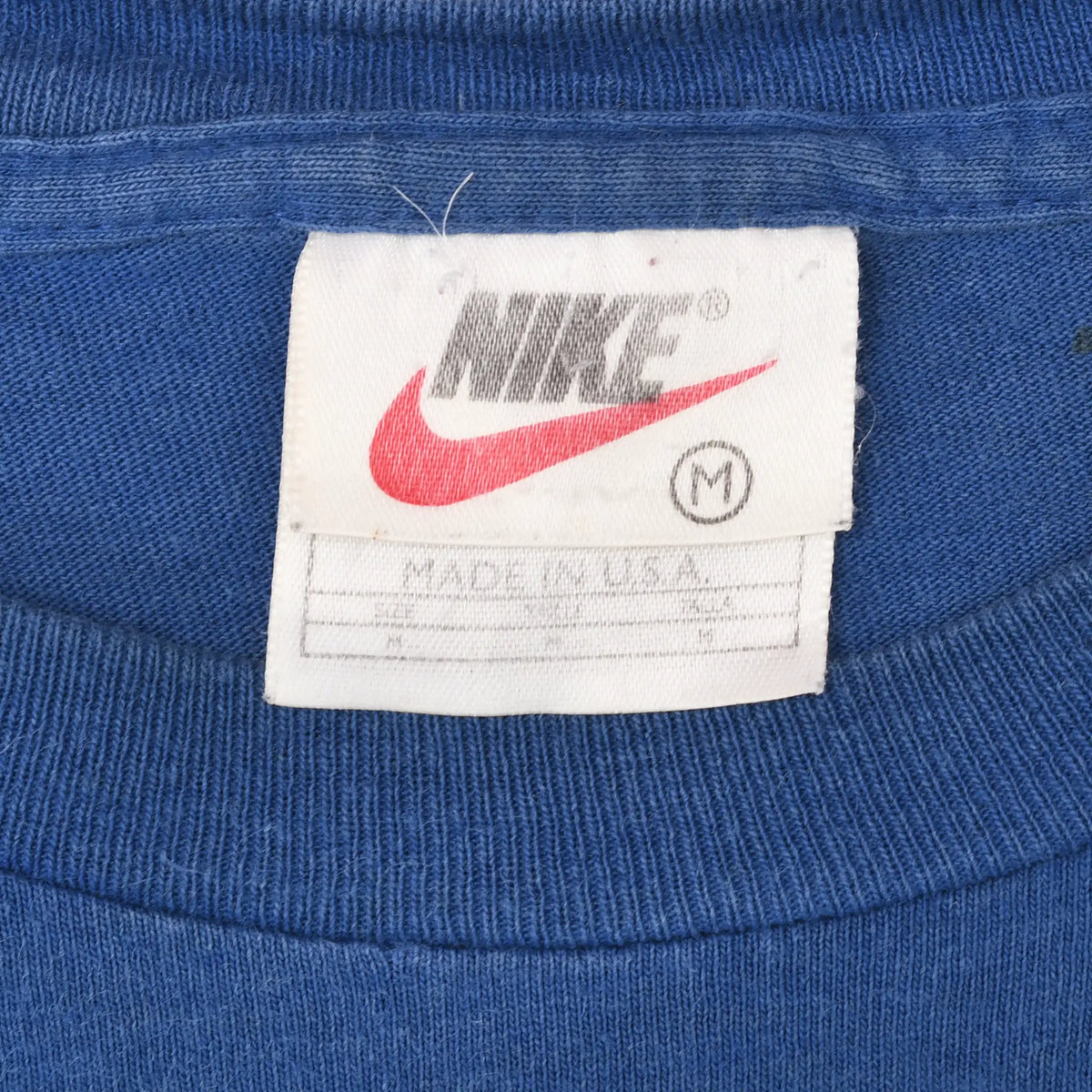 Nike neck tag on blue T-shirt showing red Swoosh, medium size, and Made in USA text