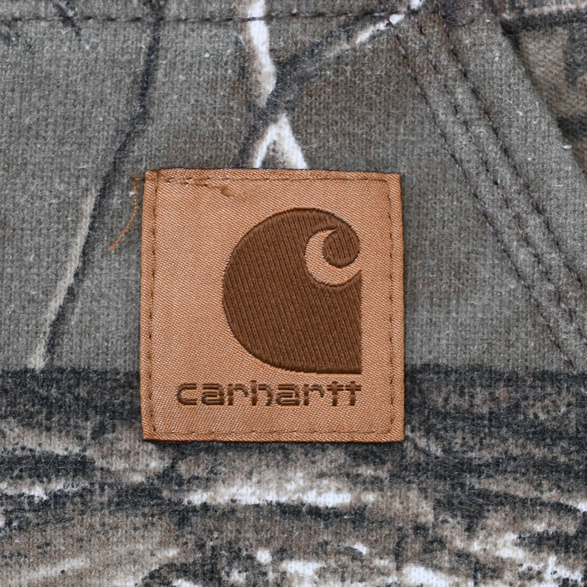 Close-up of brown Carhartt logo patch on the camo kangaroo pocket