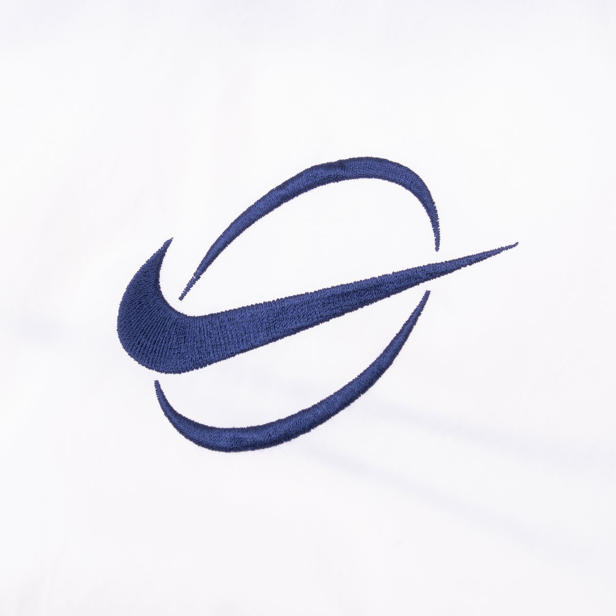 Close-up of navy Nike Swoosh embroidery on white chest panel