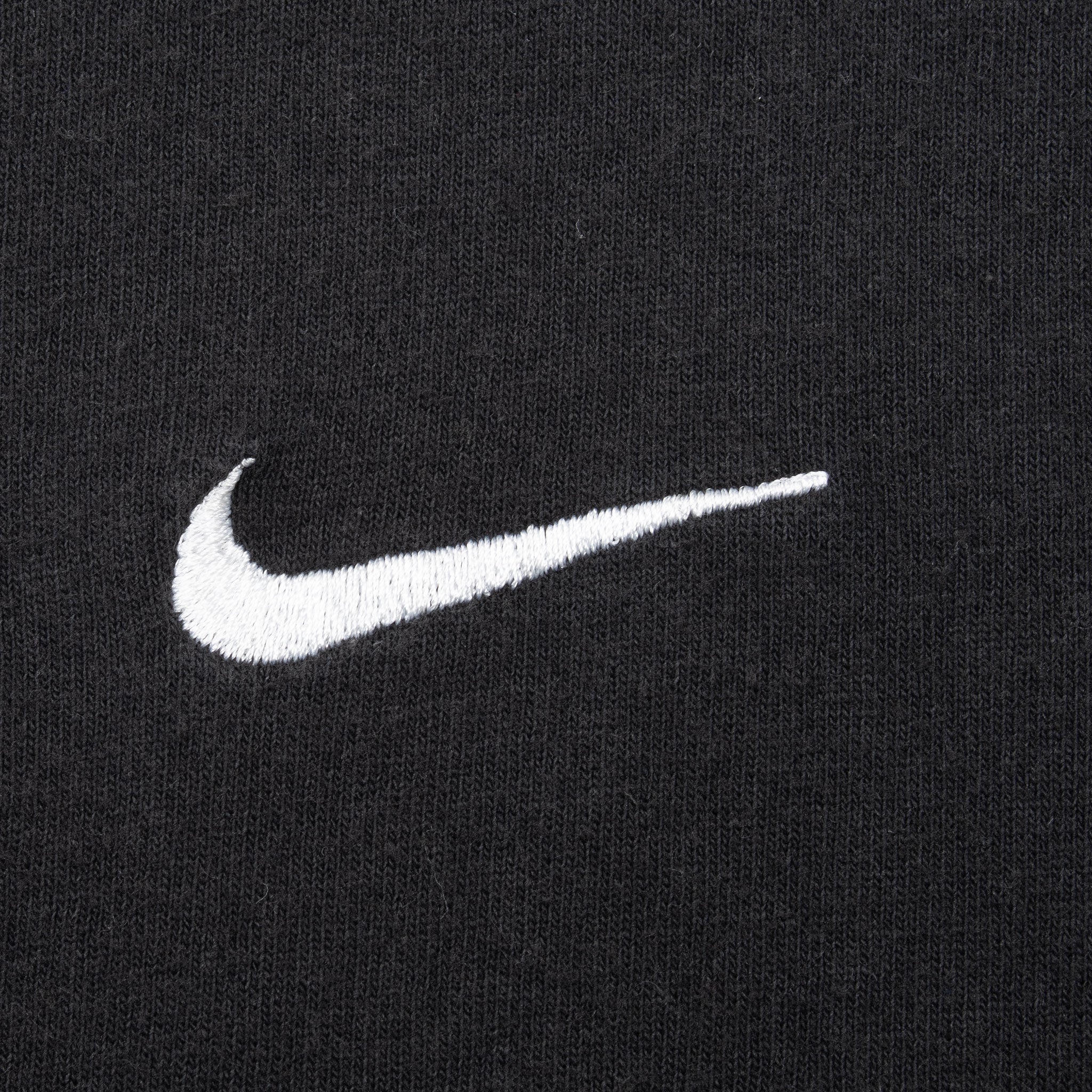 Close-up of white embroidered Nike Swoosh on black fabric