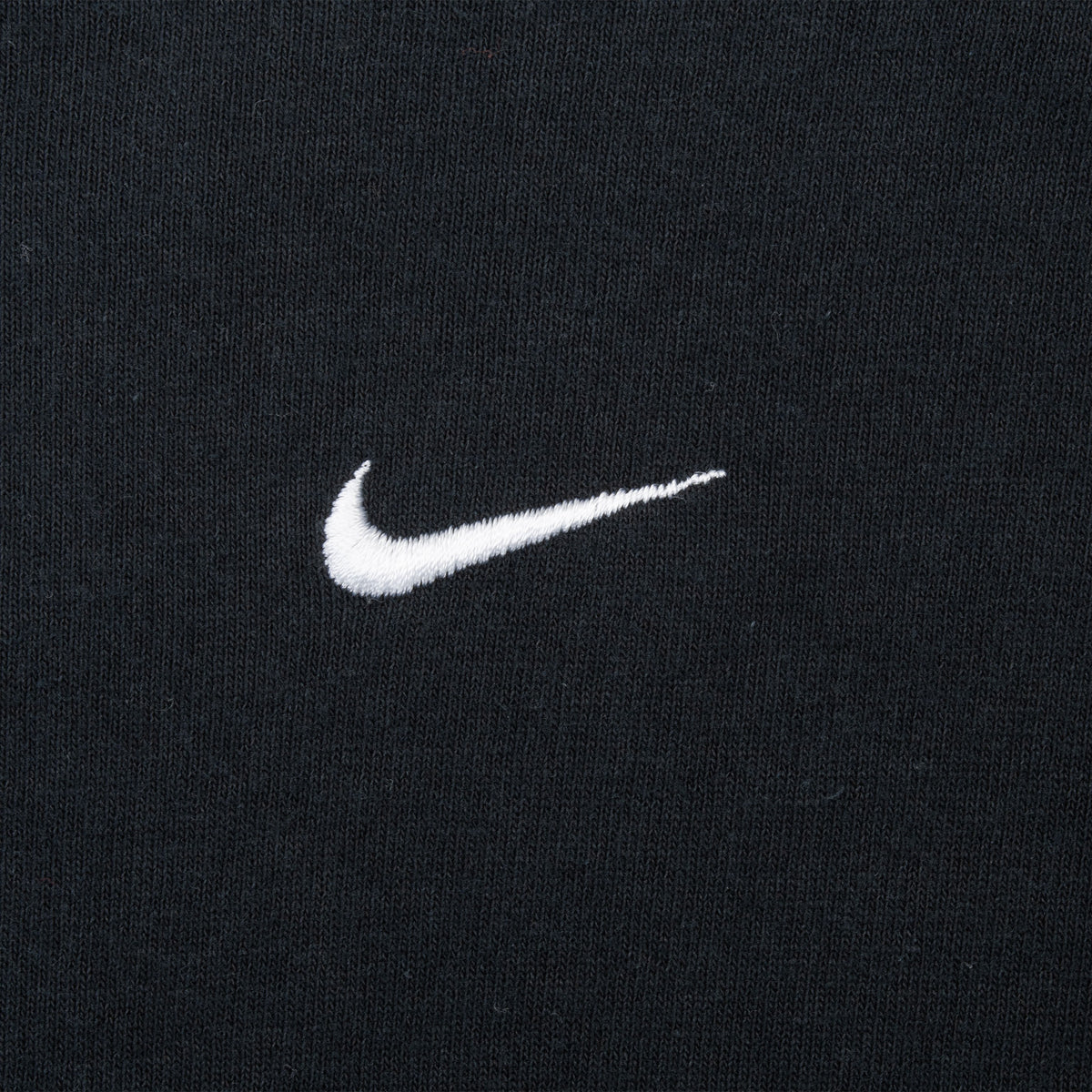 Close-up of white embroidered Nike Swoosh on black chest fabric