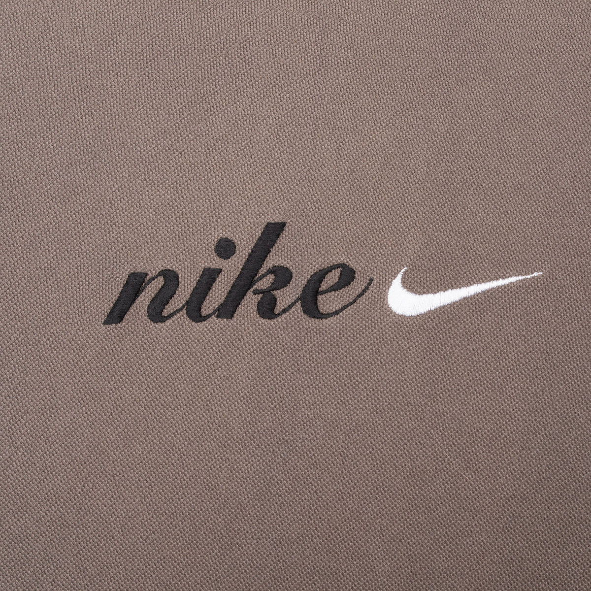 Close-up of black Nike spellout embroidery and white Swoosh on brown fabric