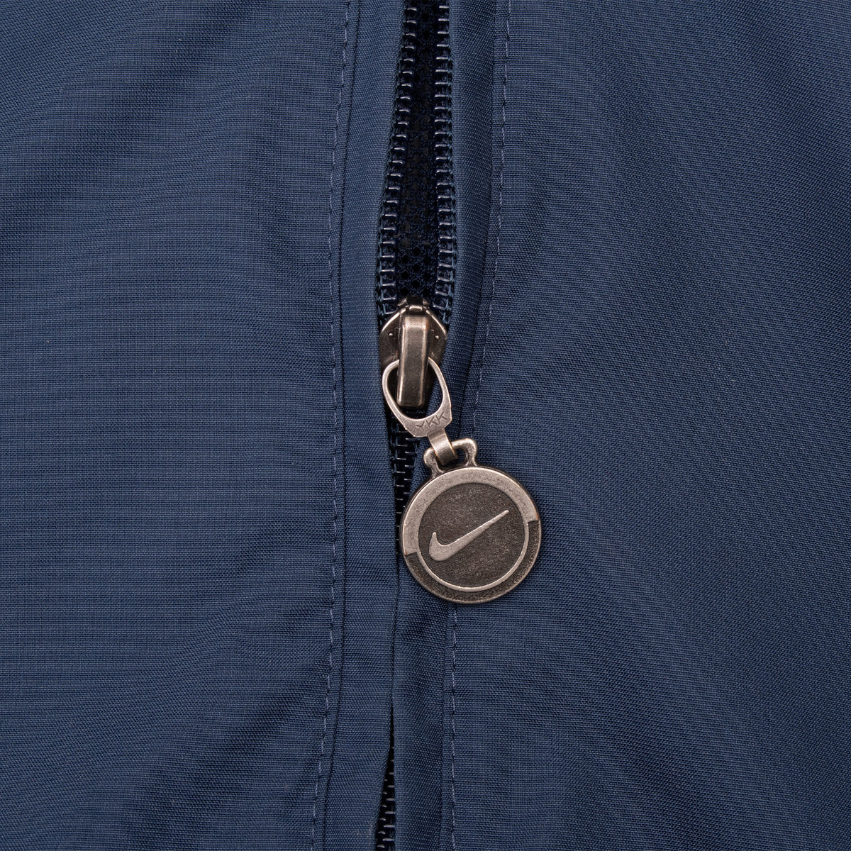 Close-up of Nike Swoosh medallion zipper pull on navy windbreaker