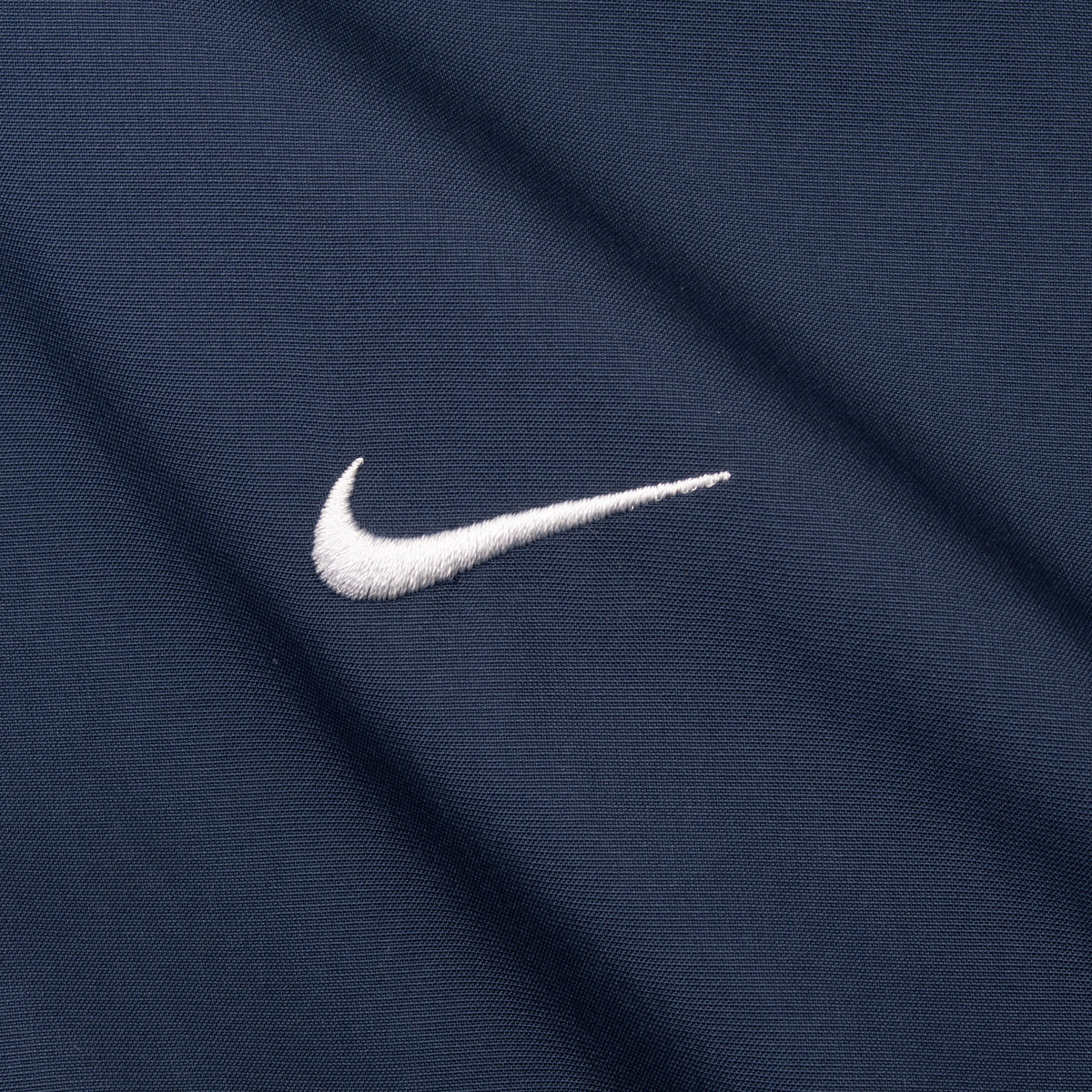 Close-up of white embroidered Nike Swoosh on navy jacket fabric