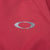 Close-up of gray Oakley ellipse chest logo on burgundy windbreaker