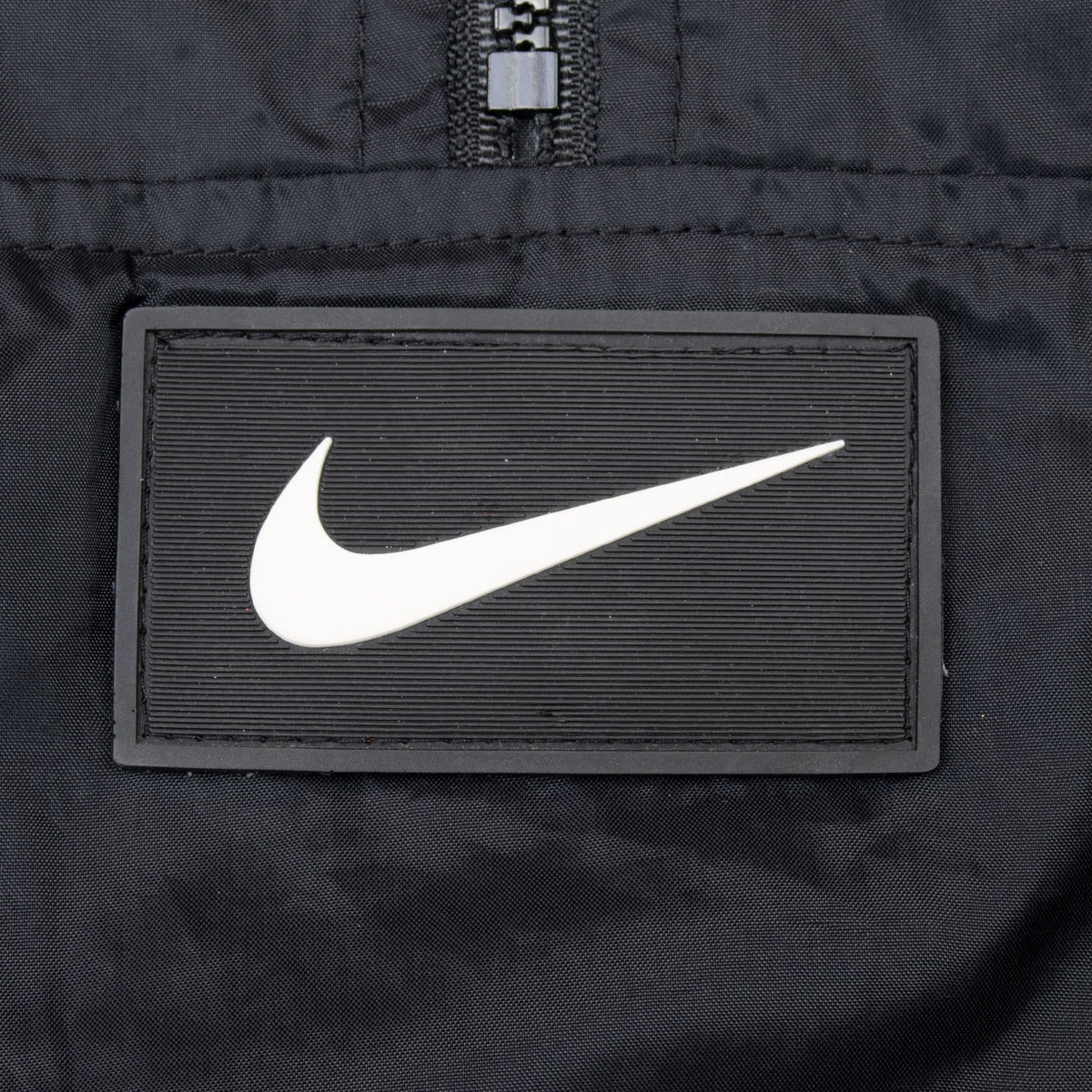 Close-up of centered white Nike Swoosh patch on black windbreaker