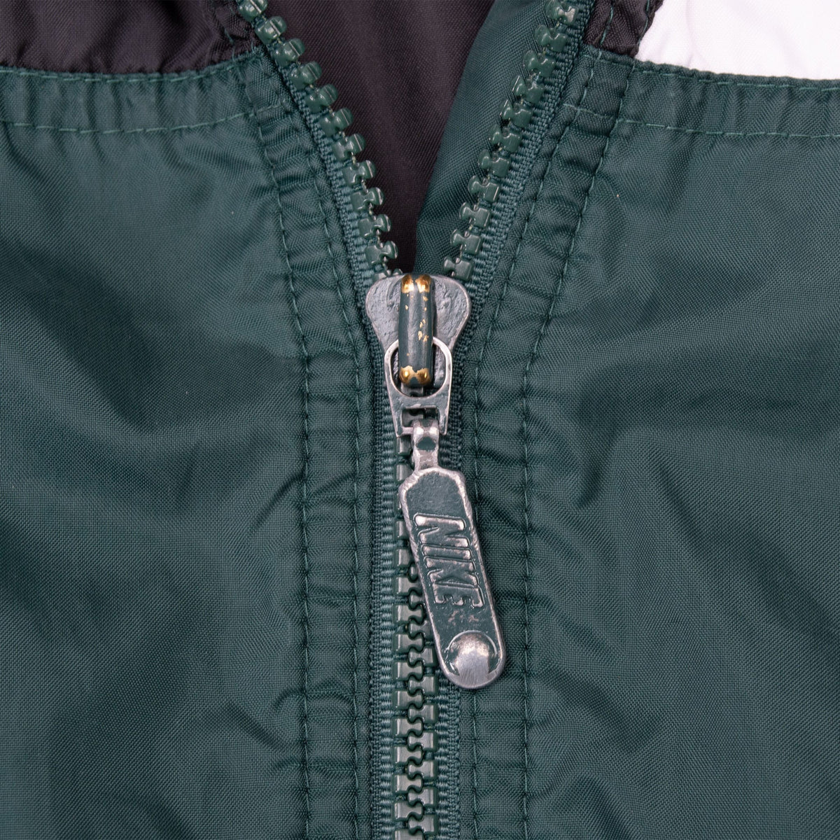 Close-up of Nike-branded metal zipper pull on green windbreaker