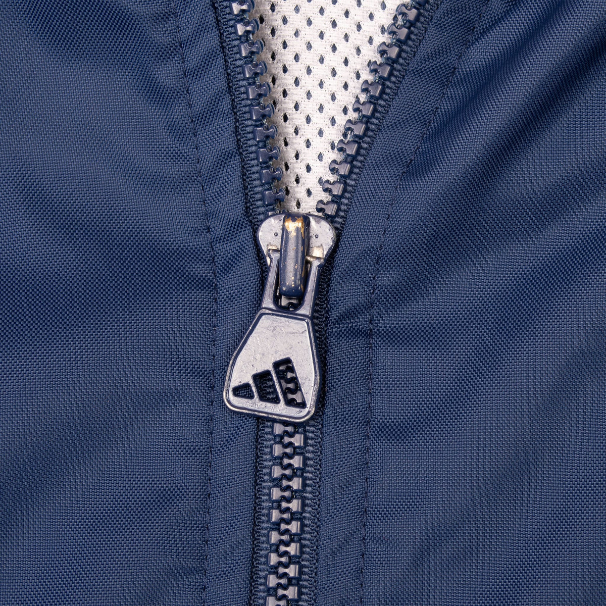 Close-up of Adidas logo zipper pull on navy windbreaker