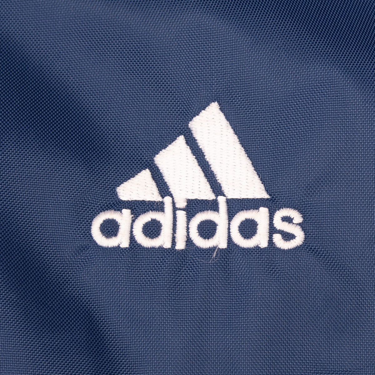Close-up of white embroidered Adidas chest logo on navy fabric