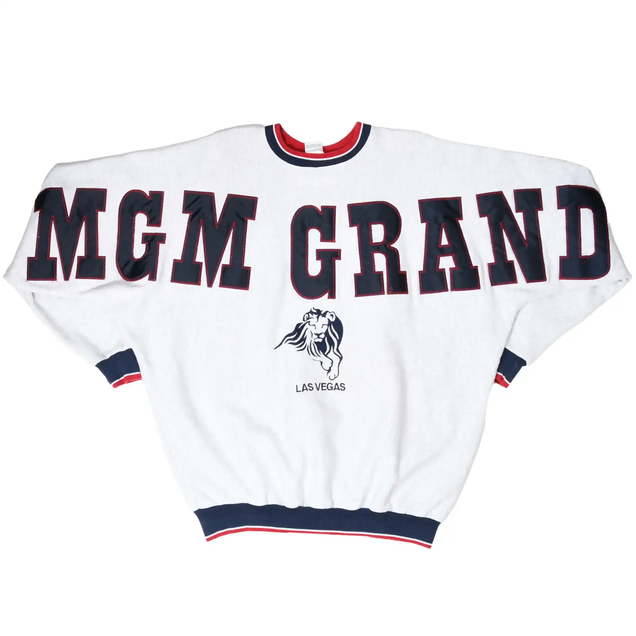 A white vintage crewneck sweatshirt featuring 'MGM GRAND' in large navy blue block letters with red trim across the chest, and a small Las Vegas lion graphic below. The sweatshirt has navy and red ribbed trim at the collar, cuffs, and hem.