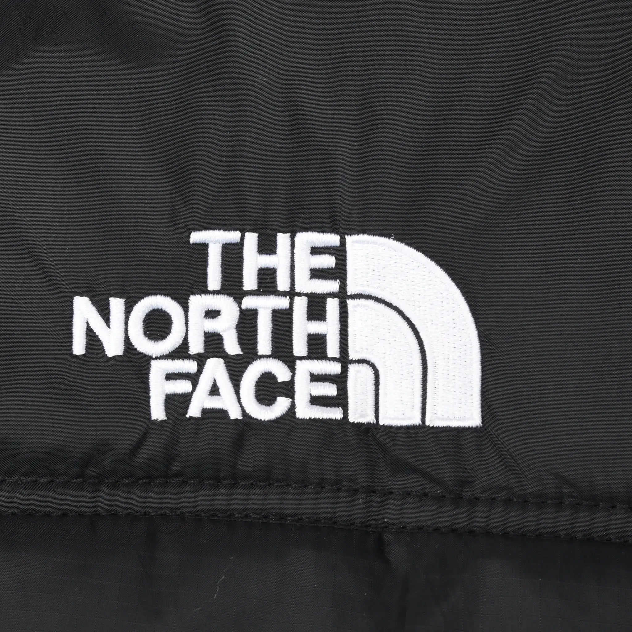 Close-up of white The North Face logo embroidery on black jacket shell