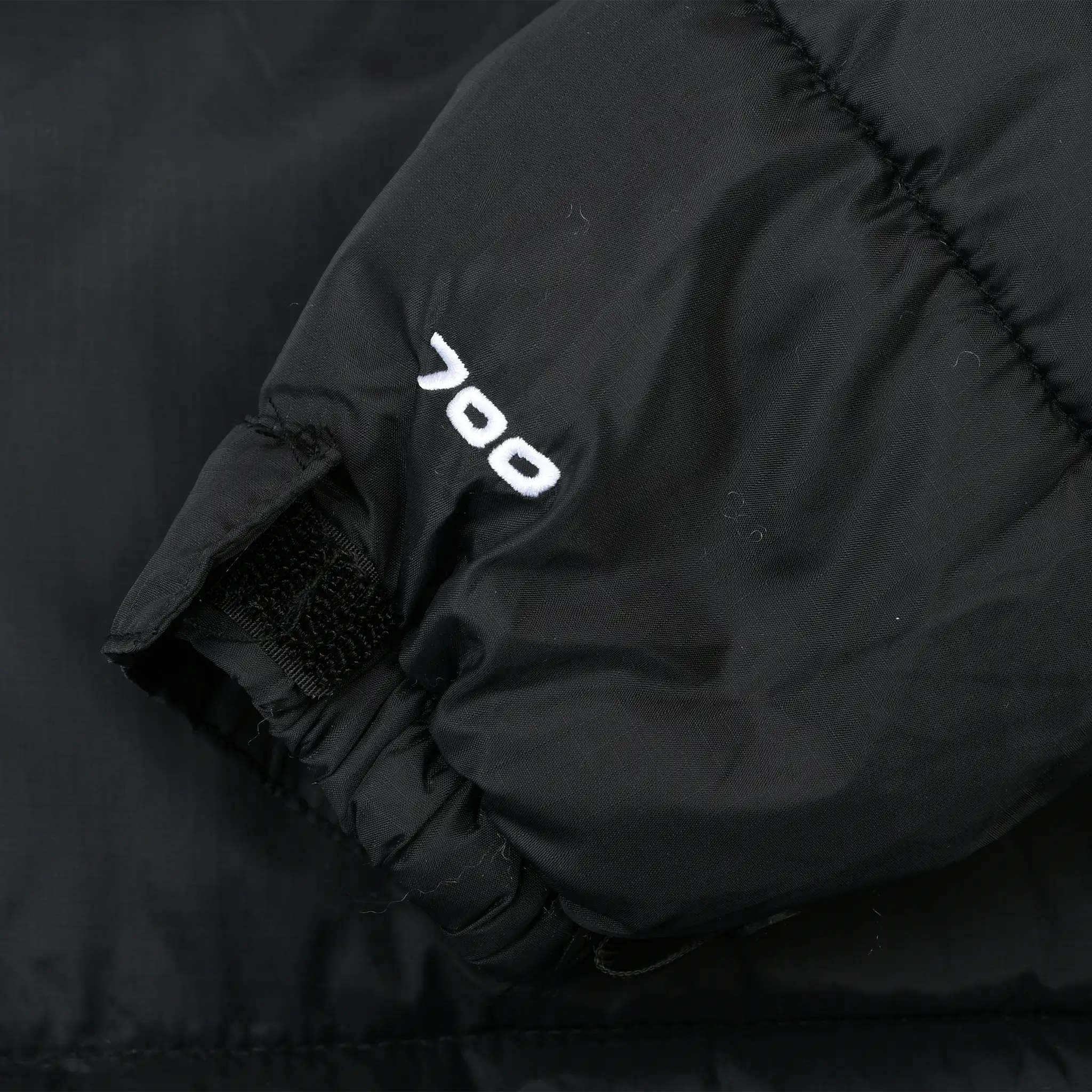 Close-up of white 700 embroidery and adjustable cuff on black jacket sleeve