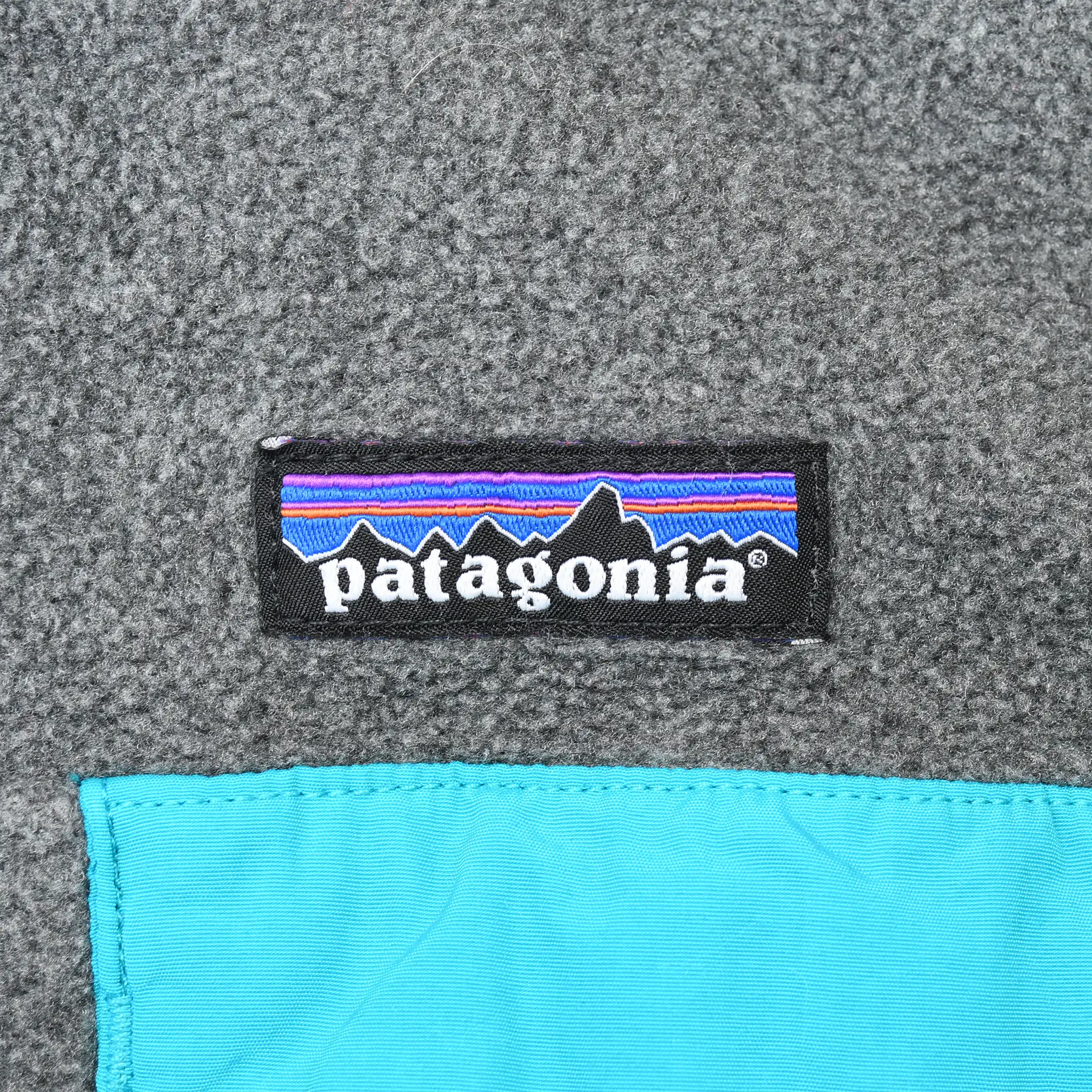 Patagonia logo above turquoise chest pocket on dark grey fleece