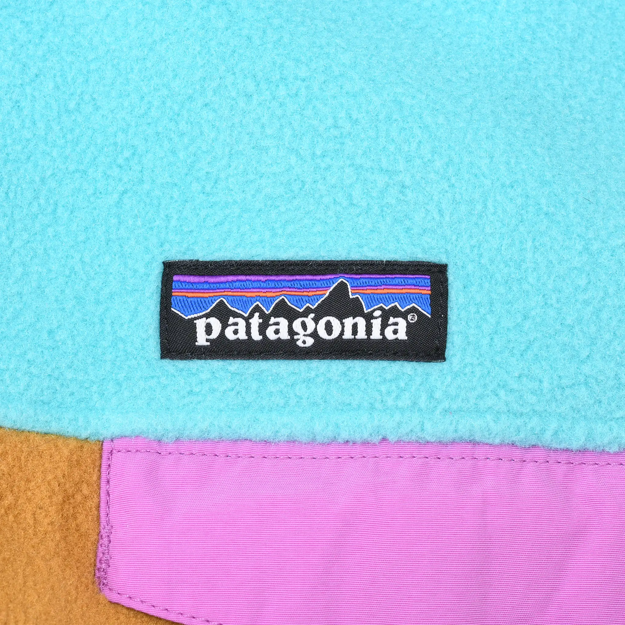 Patagonia logo patch above the pink chest pocket flap on turquoise fleece