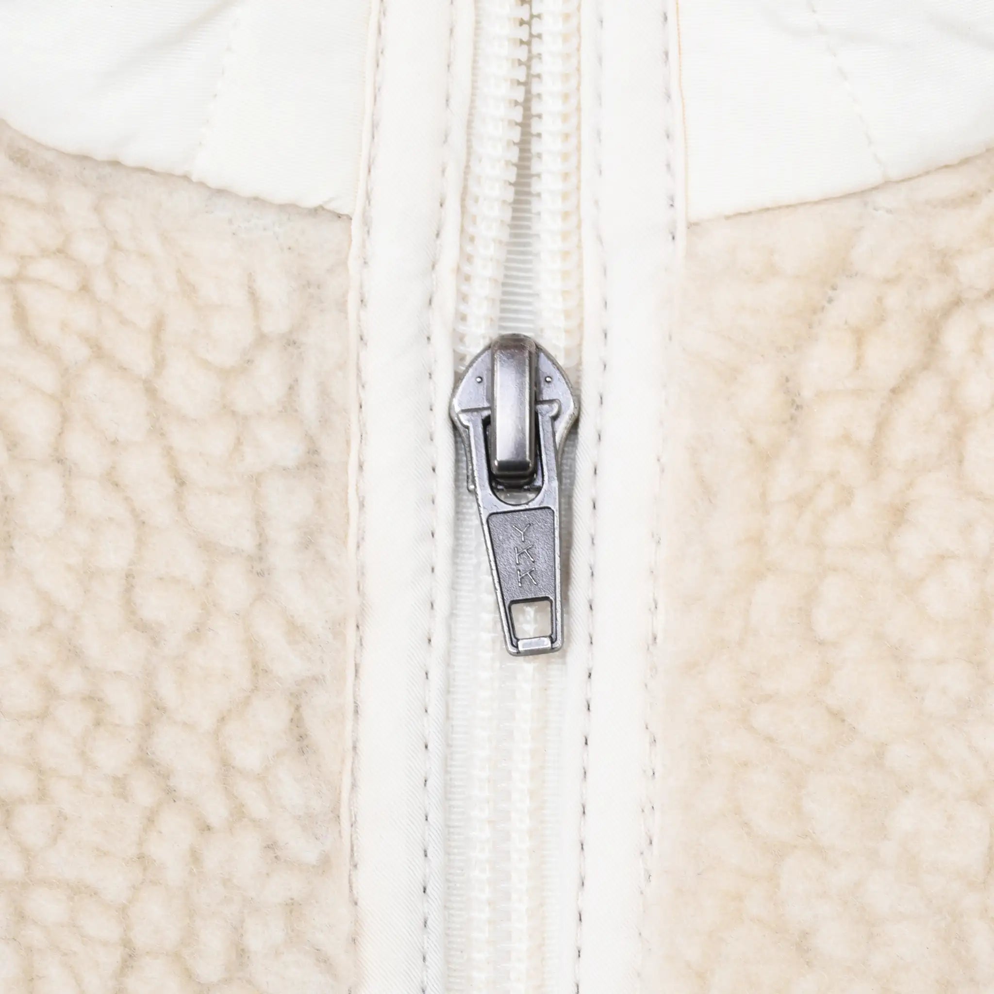 Close-up of metal zipper pull and white trim on beige fleece jacket