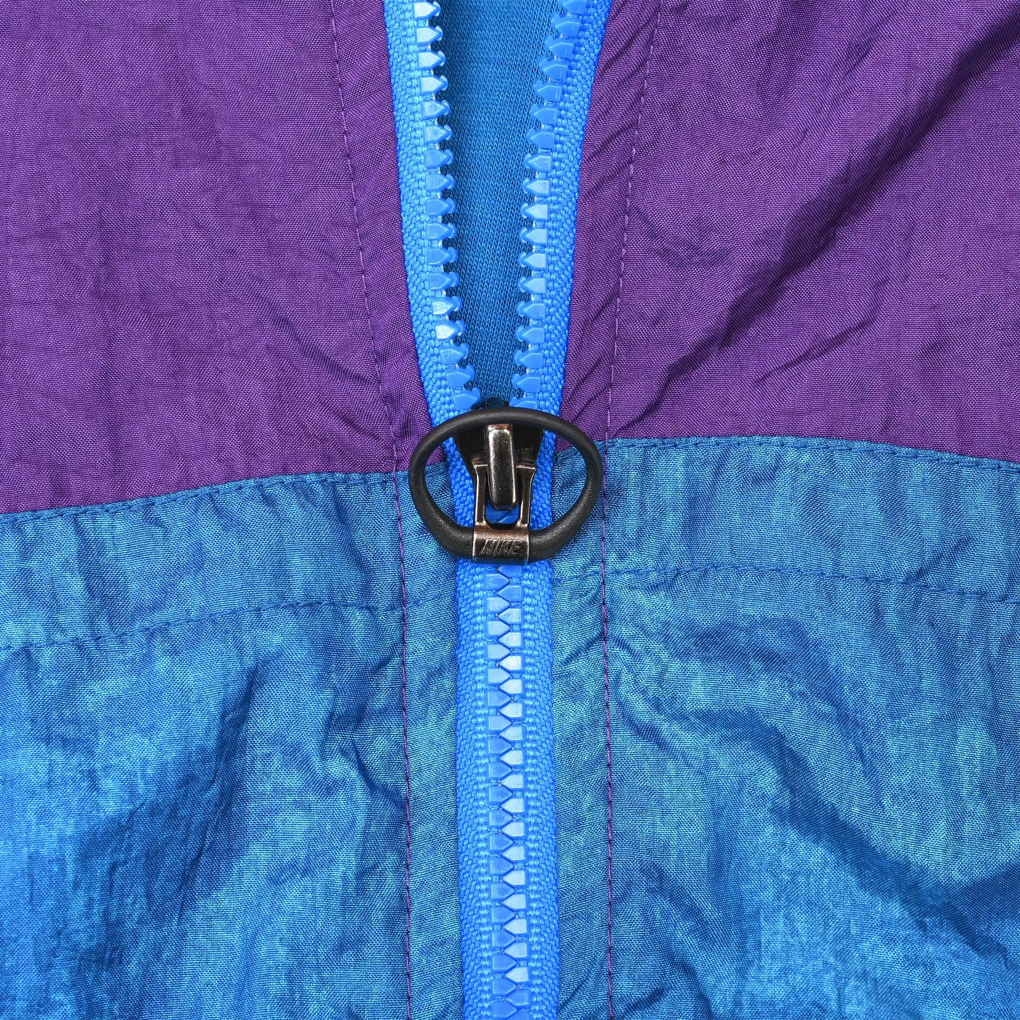 Close-up of blue front zipper with black ring pull and purple-blue color blocking