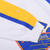 Sleeve detail with white cuff, yellow and blue stripes, and a small mark indicated by an arrow sticker