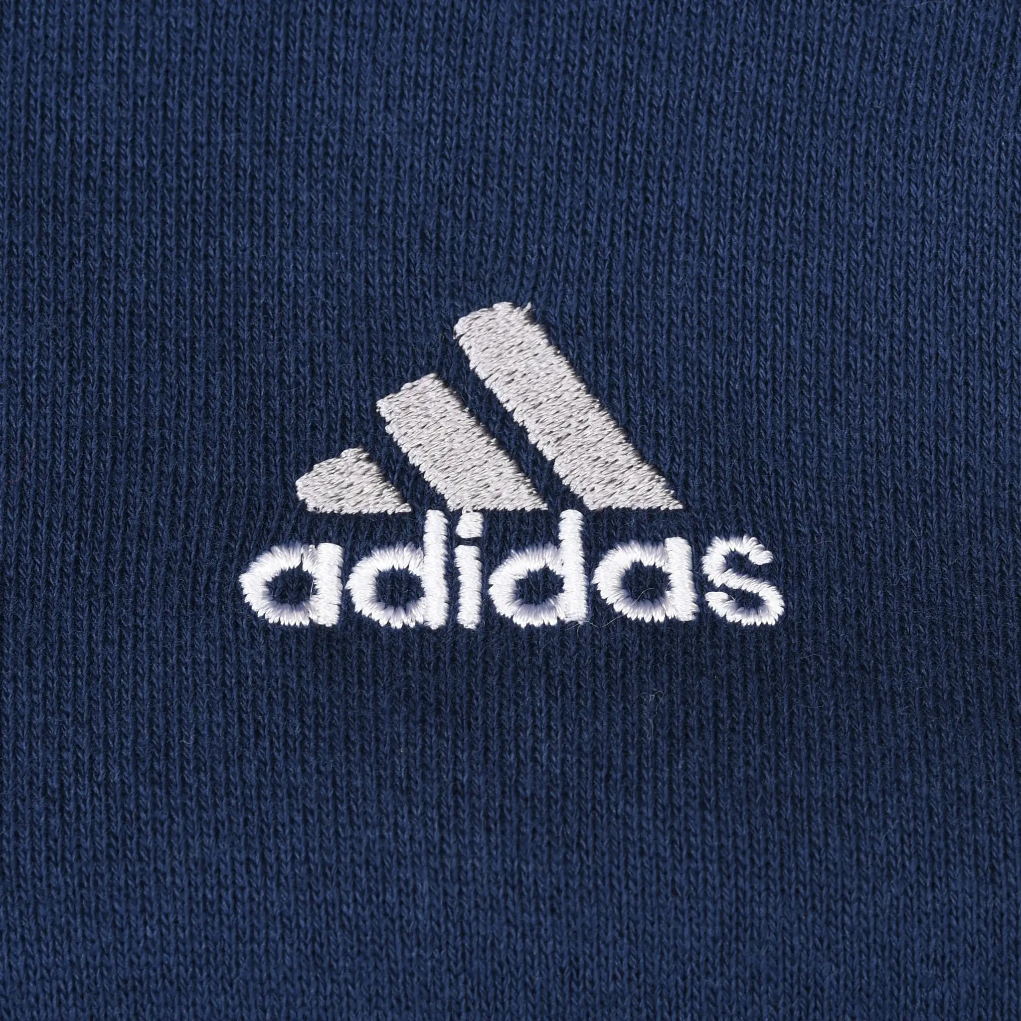 Close-up of white Adidas logo embroidery on navy blue hoodie chest