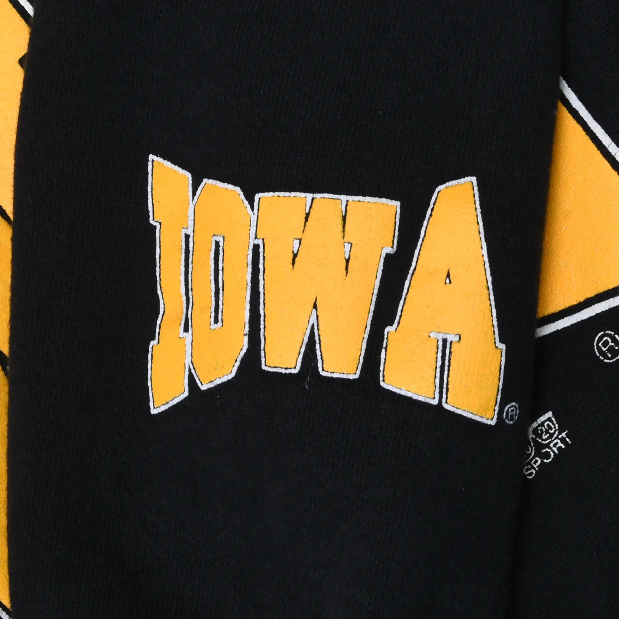 Close-up of small gold Iowa wordmark printed on black sweatshirt sleeve