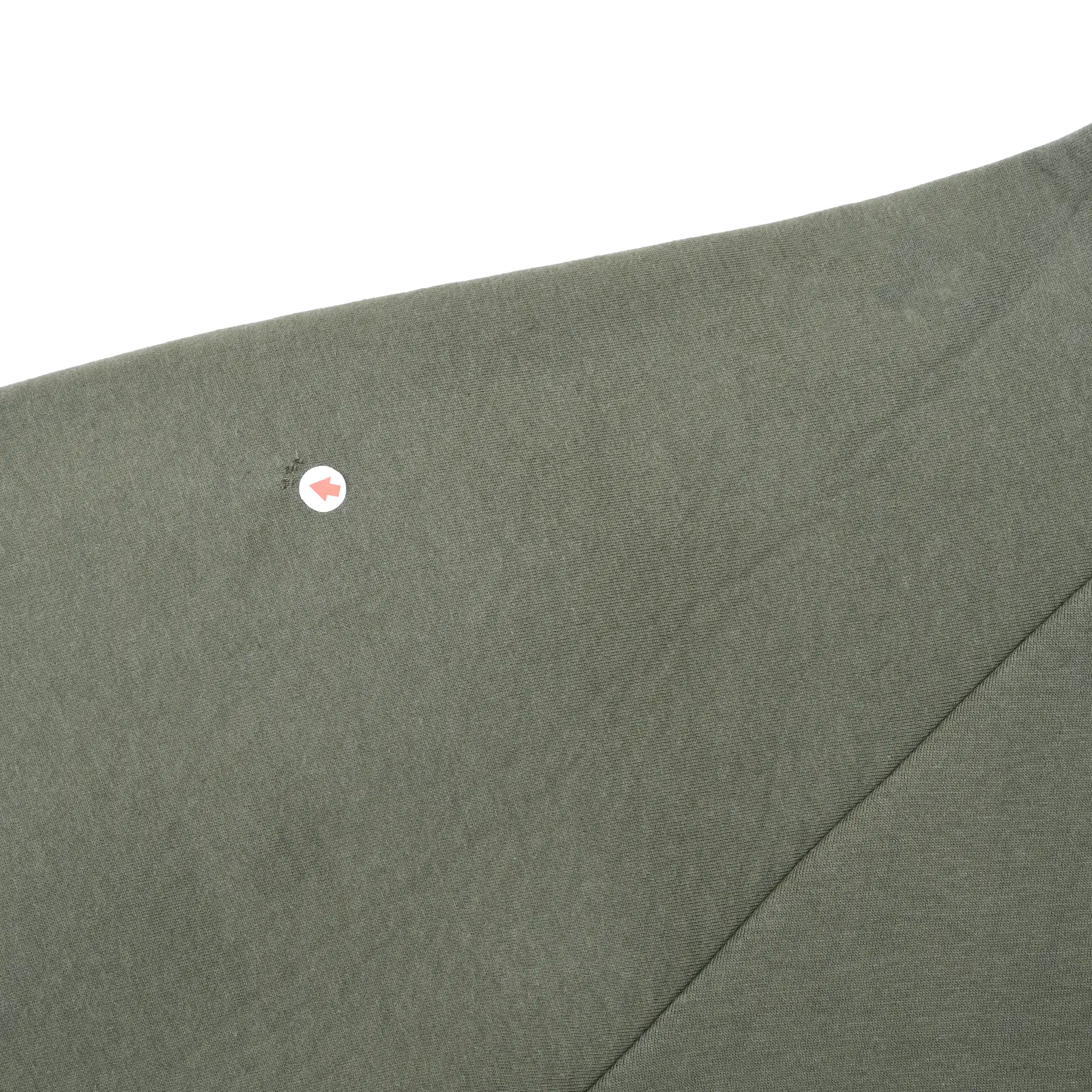 Close-up of olive green sleeve fabric with an arrow marking a small spot